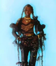 Model with braided hair wearing black lace top and dark shiny trousers against light blue background