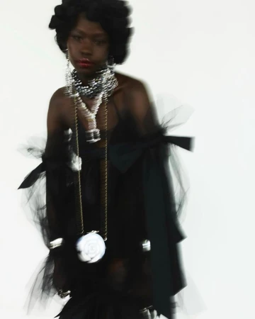 Elegant portrait of a Black woman in a tulle dress with statement jewelry and a purse with a floral design on a white background.