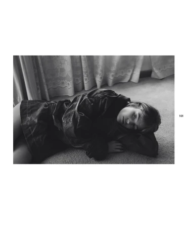 Black and white portrait of a model lying on the floor in a loose jacket with curtains in the background. Editorial fashion photography.