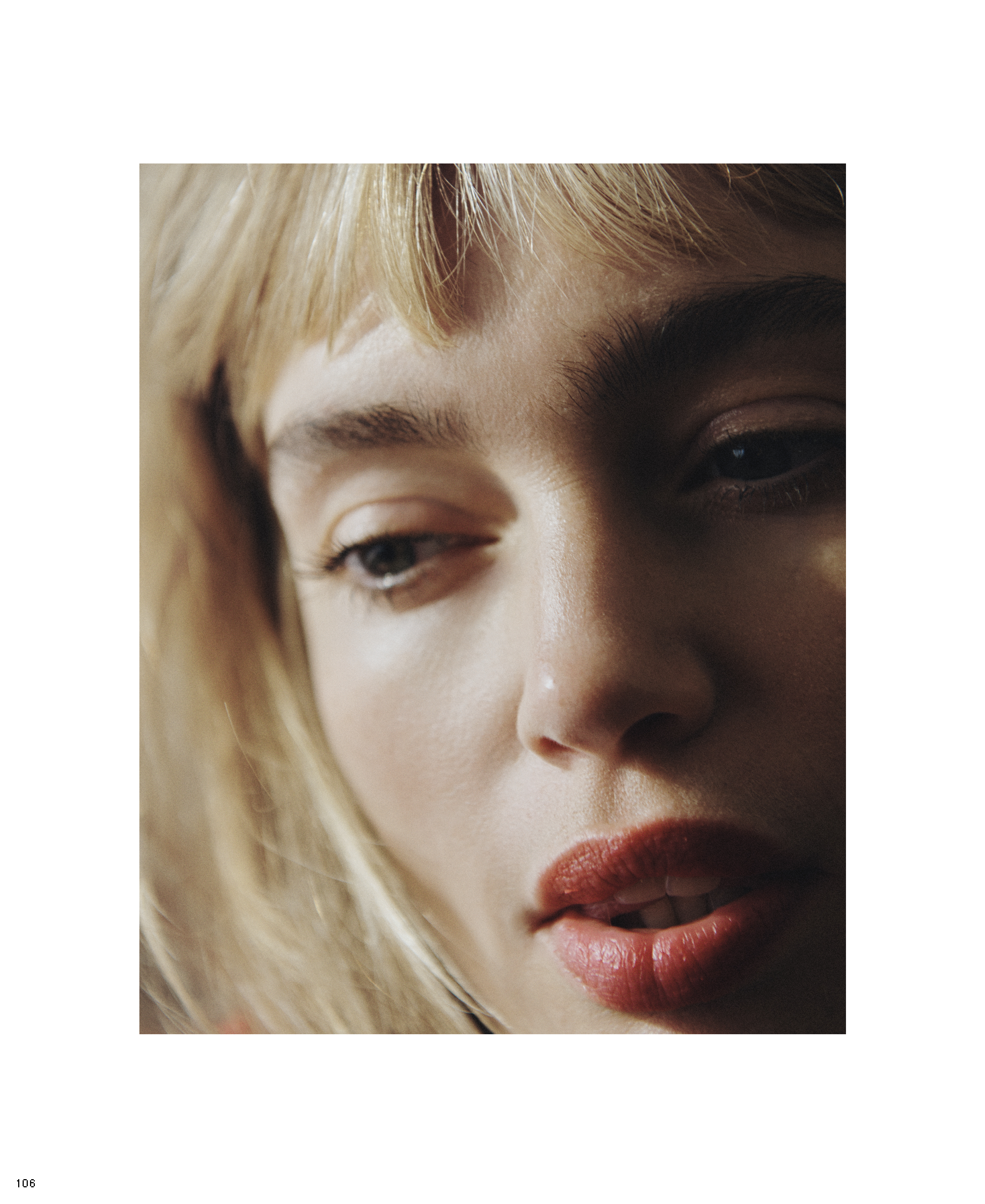 Close-up portrait of a young adult female with blonde hair and red lipstick. The shot is softly lit and focuses on her facial features.