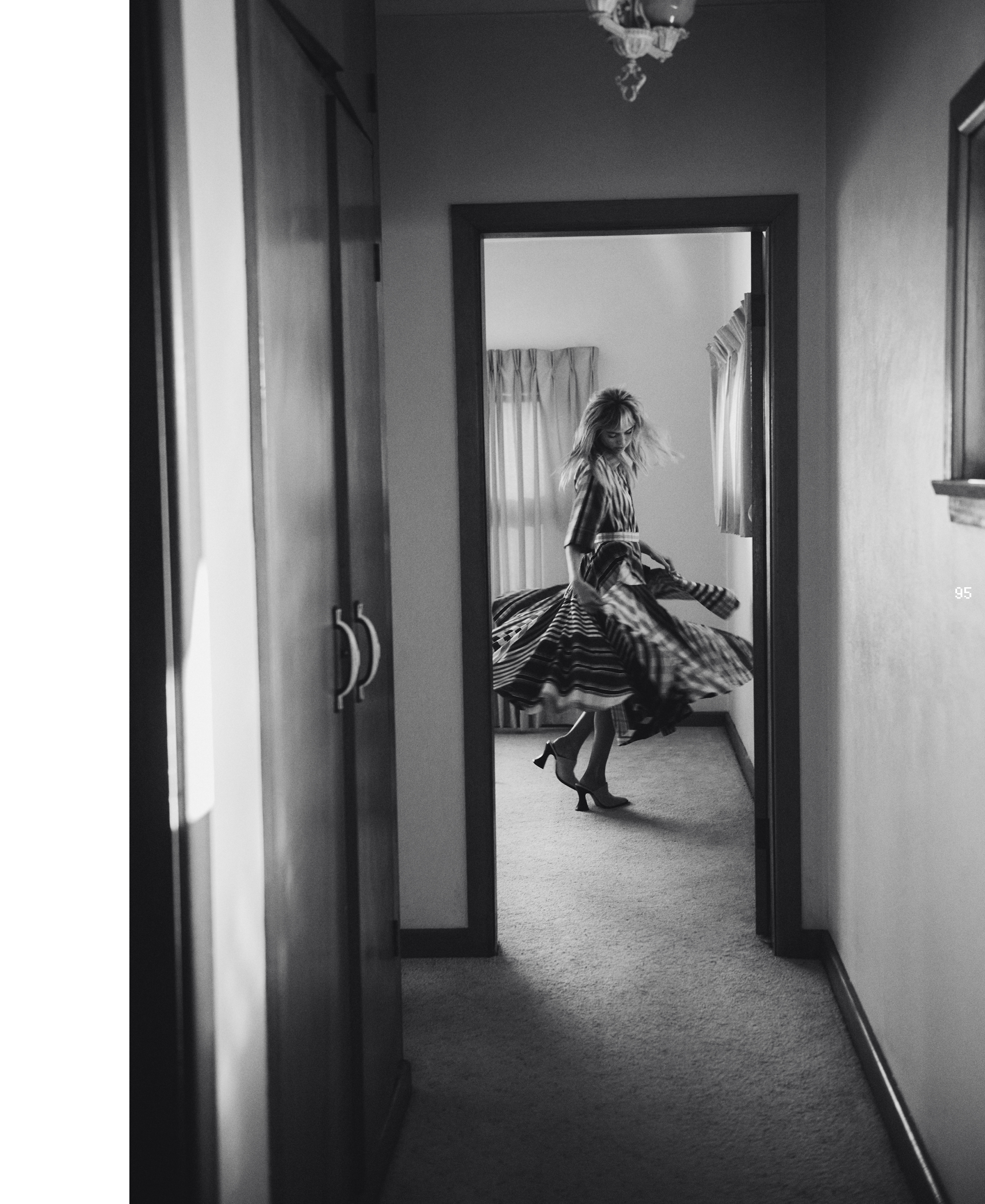A woman in a striped dress spins in a hallway. The black-and-white image shows her motion and the interior's architecture.