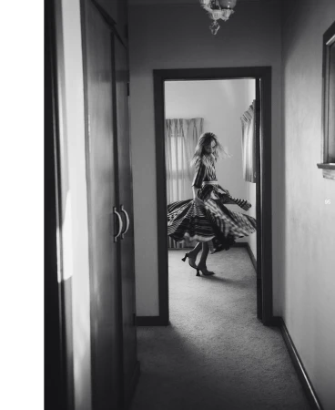 A woman in a striped dress spins in a hallway. The black-and-white image shows her motion and the interior's architecture.