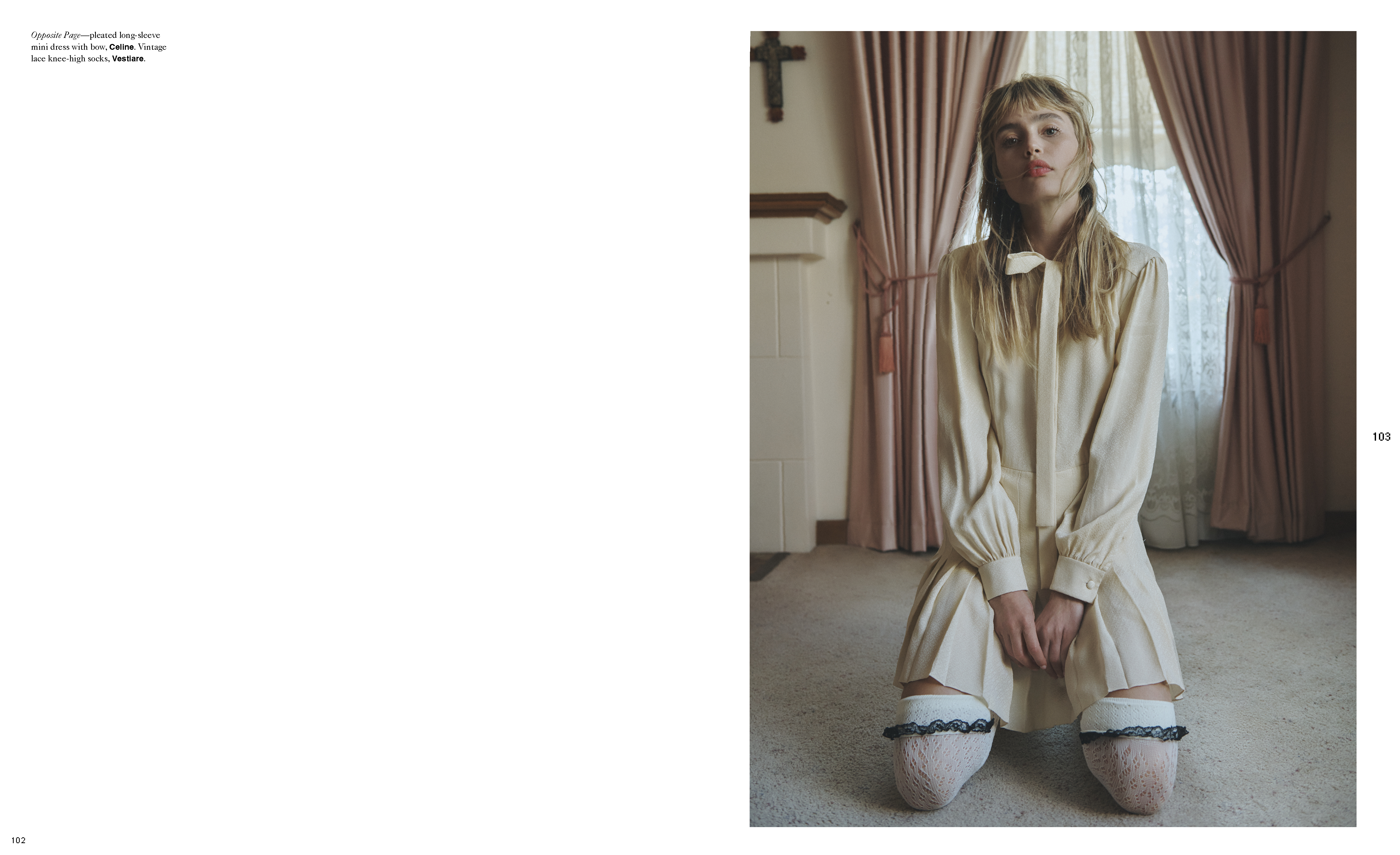 A young adult female model kneels in a dress and knee-high socks indoors, illuminated by soft light near a window and muted pink curtains.