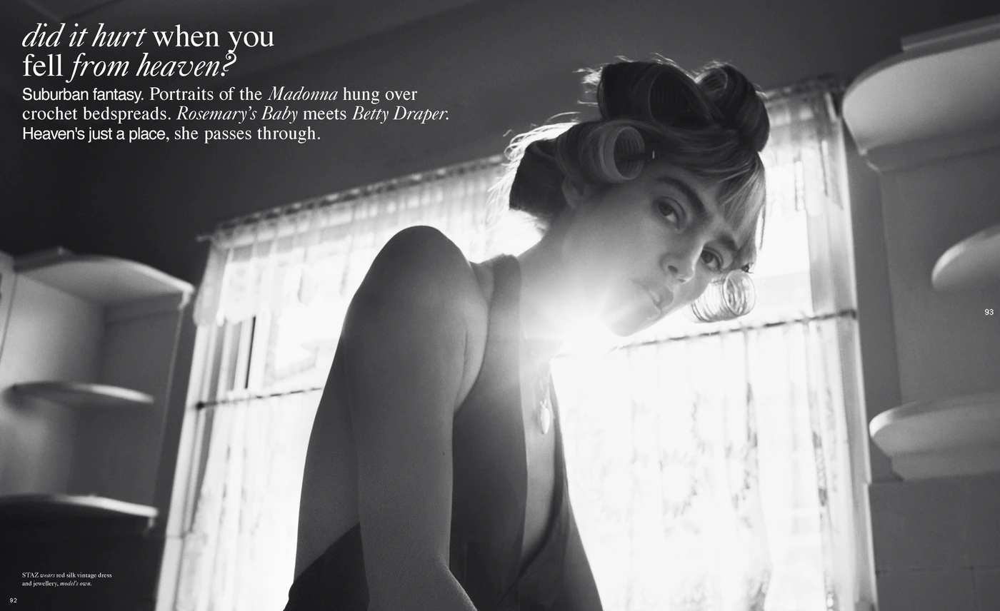 Black and white editorial portrait of a woman with hair rollers in a domestic interior with bright window light.
