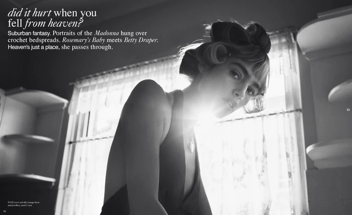Black and white editorial portrait of a woman with hair rollers in a domestic interior with bright window light.
