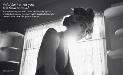 Black and white editorial portrait of a woman with hair rollers in a domestic interior with bright window light.