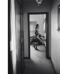 Model spinning in a patterned dress down a domestic hallway captured in monochrome