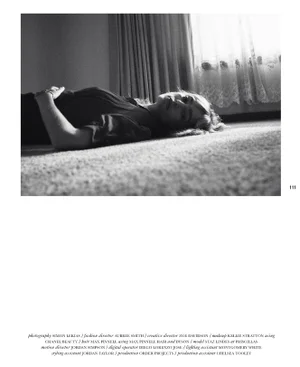 Monochrome editorial portrait of a woman lying on a carpeted floor near a window with sheer curtains.