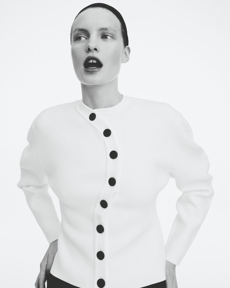 Monochrome portrait of a woman in a white cardigan with black buttons, looking off to the side with her mouth slightly open.