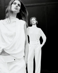 Black and white portrait of two models wearing white outfits against a dark background, photographed by Robin Galiegue for Zara.