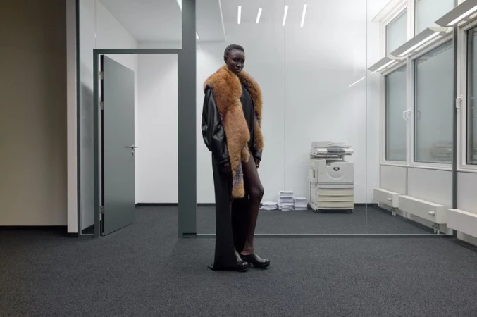 Model wearing a long black coat with a fur stole standing in a modern office interior