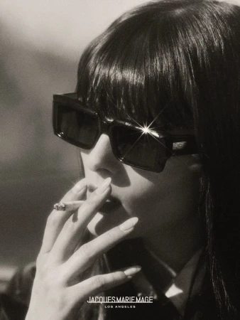 Adult woman with sunglasses smokes a cigarette in a close-up portrait. Jacques Marie Mage Los Angeles brand is visible at the bottom.