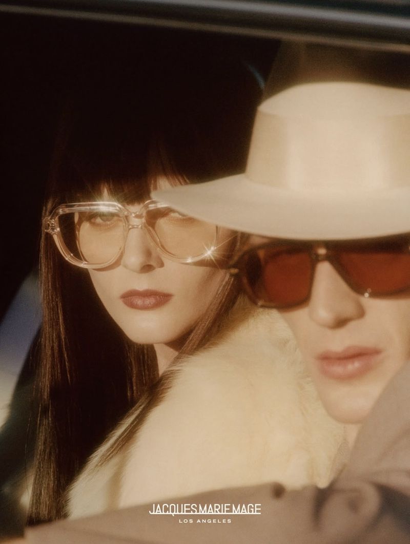 Close-up fashion shot of an adult female and male wearing eyewear, hats and fur coats in a vehicle with a warm, vintage colour grade.