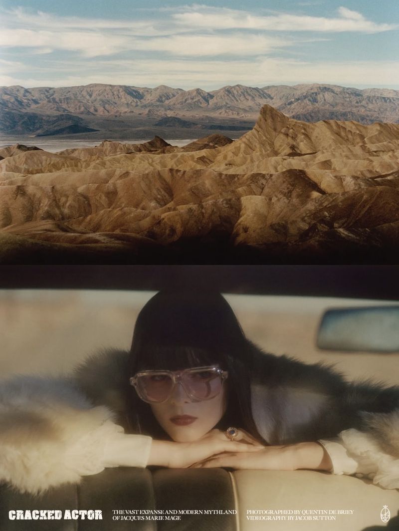 Model wearing tinted sunglasses and dark hood leaning over a car interior with desert mountain landscape visible above