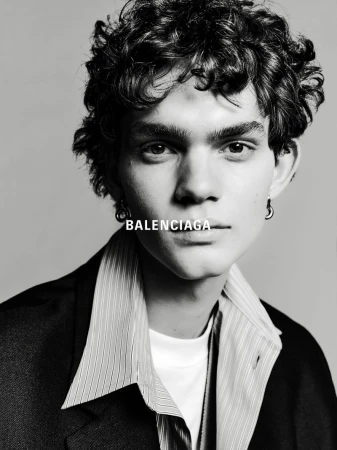 Black and white portrait of a young adult male wearing a blazer and striped shirt, featuring the Balenciaga logo near his neck.