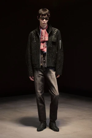 Model wearing a black embroidered jacket, patterned scarf, and dark jeans against a dark background for Masu lookbook.
