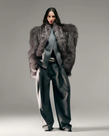 A female fashion model poses in a grey fur coat, grey top, wide-legged grey trousers, and a silver belt against a neutral backdrop.