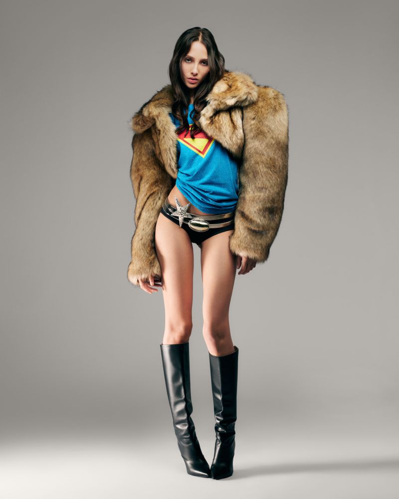 Model Yasmin Wijnaldum wearing a furry brown coat and blue t-shirt against a plain grey studio backdrop