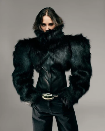 Model Yasmin Wijnaldum wearing a black faux fur jacket and dark trousers against a plain grey background for David Koma Pre-Fall 2026.