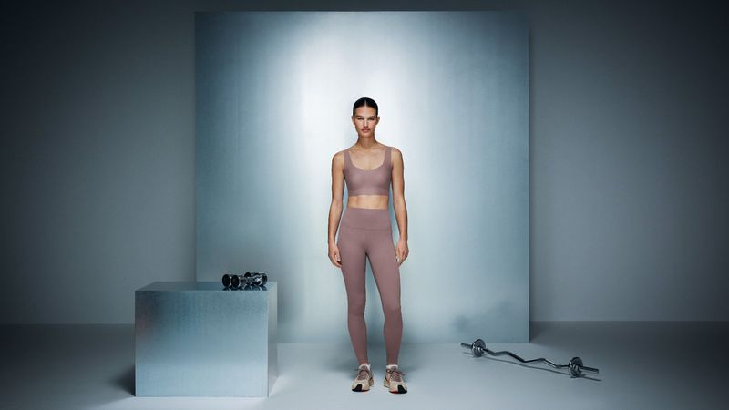 A slender woman in a matching bra top and leggings poses in a studio setting with workout accessories, promoting fitness and healthy lifestyle.