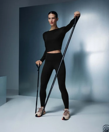 Athletic woman in black activewear using resistance band in a studio. Fitness training for upper body strength and core conditioning.