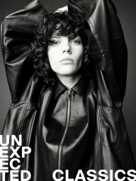 Model with curly dark hair wearing a black leather jacket with arms raised, photographed in monochrome.