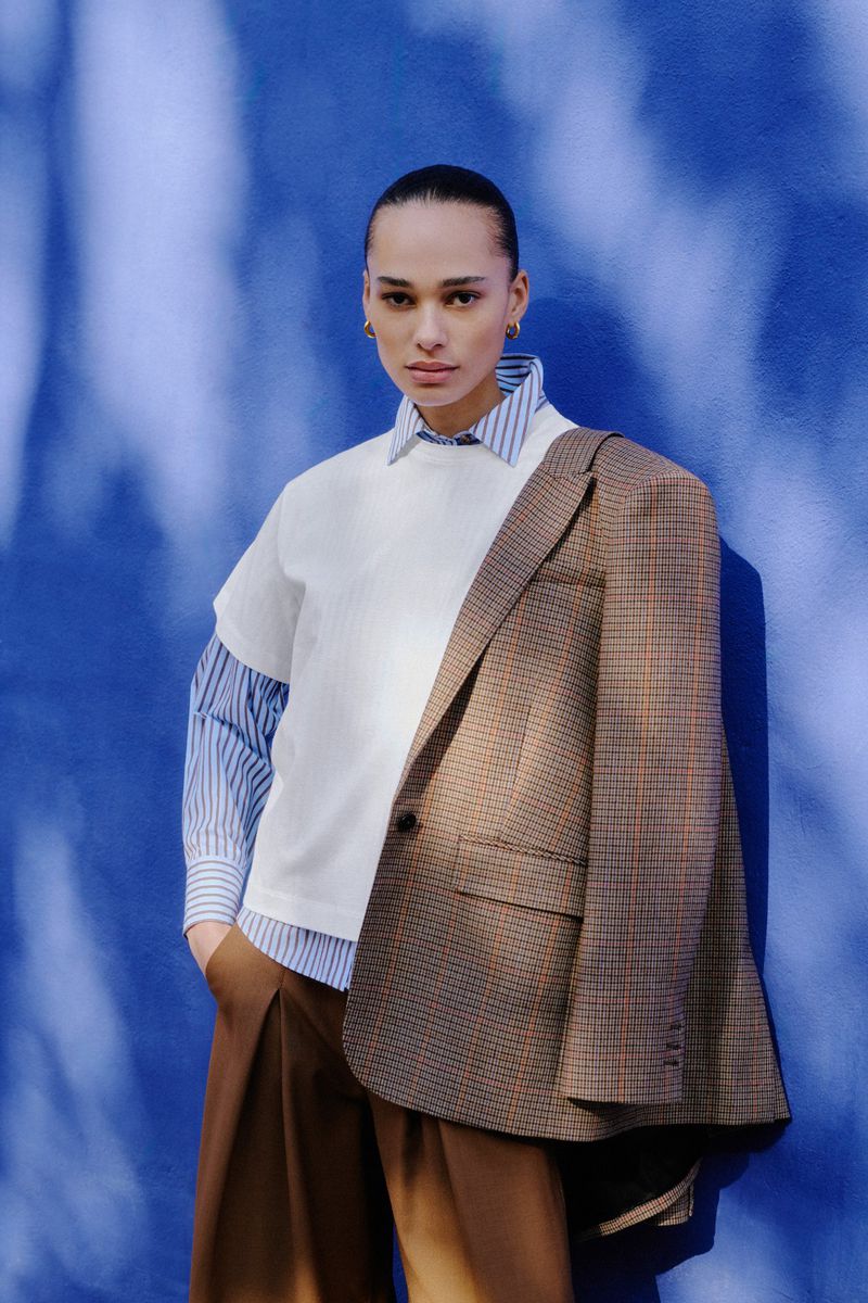 Stylish portrait of a person in a white tee and brown jacket against a blue backdrop, showcasing contemporary fashion and posing.