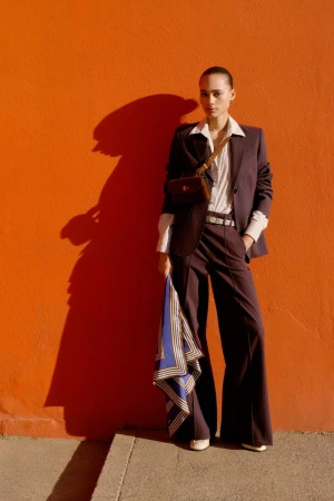 Model wearing a brown pinstripe suit and holding a blue scarf against a vibrant orange wall