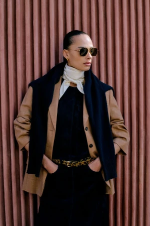 Model wearing dark sunglasses, camel blazer, and draped scarf against a ribbed terracotta background for ME+EM February Lookbook.