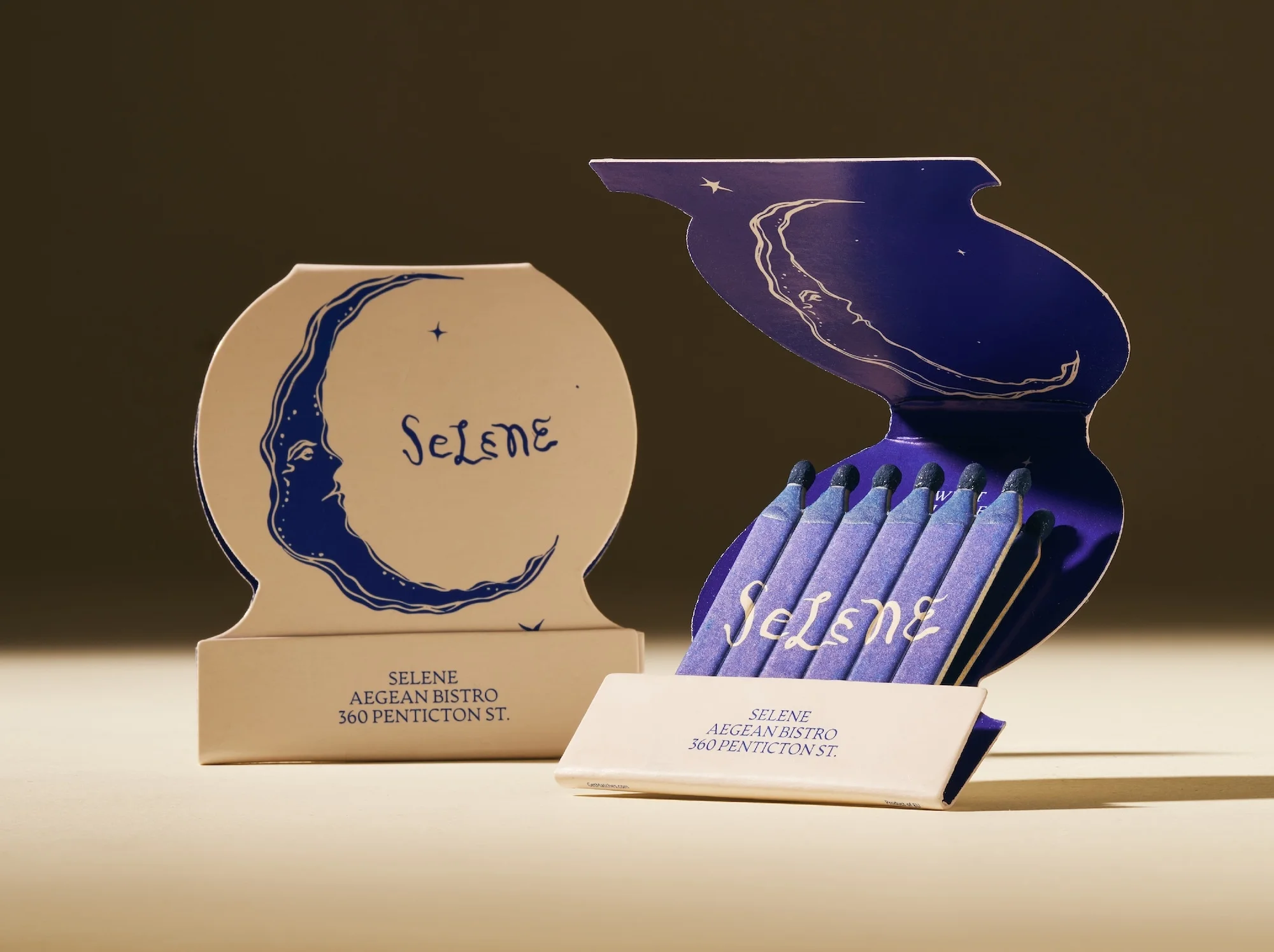 Two matchboxes are displayed, one closed and one open with blue-tipped matches, both featuring the logo for Selene Aegean Bistro.