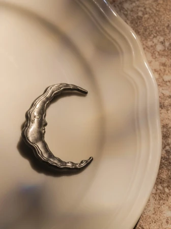 Crescent moon ornament on a white plate. The moon features a face and sits on a beige and white surface. Elegant home decoration.