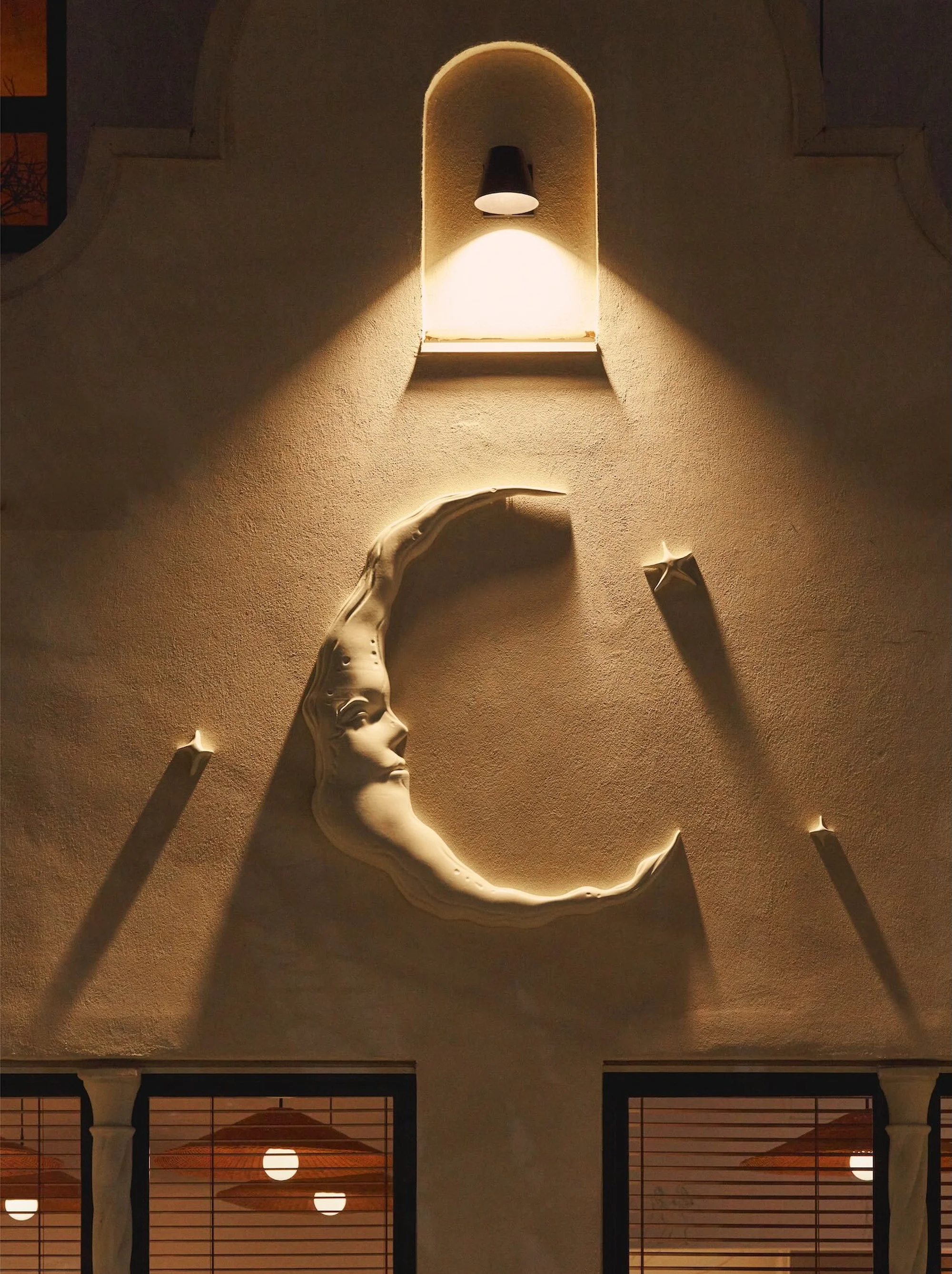 Exterior wall featuring a half-moon sculpture with a face, star-shaped lights, and warm lighting, creating a unique architectural display.
