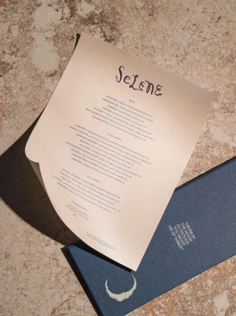 Overhead shot of a Selene menu and a blue box with a crescent moon and text on a mottled beige surface.