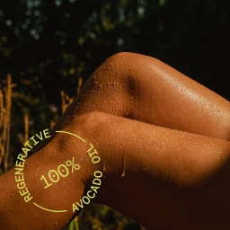 Close-up of sun-kissed legs covered in water droplets with overlaid yellow text reading 100 percent avocado oil by Acure