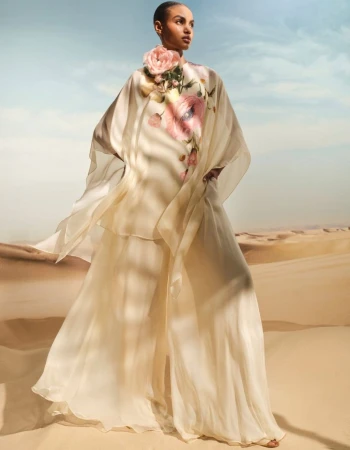 Model in cream floral caftan standing against sand dunes under an open sky
