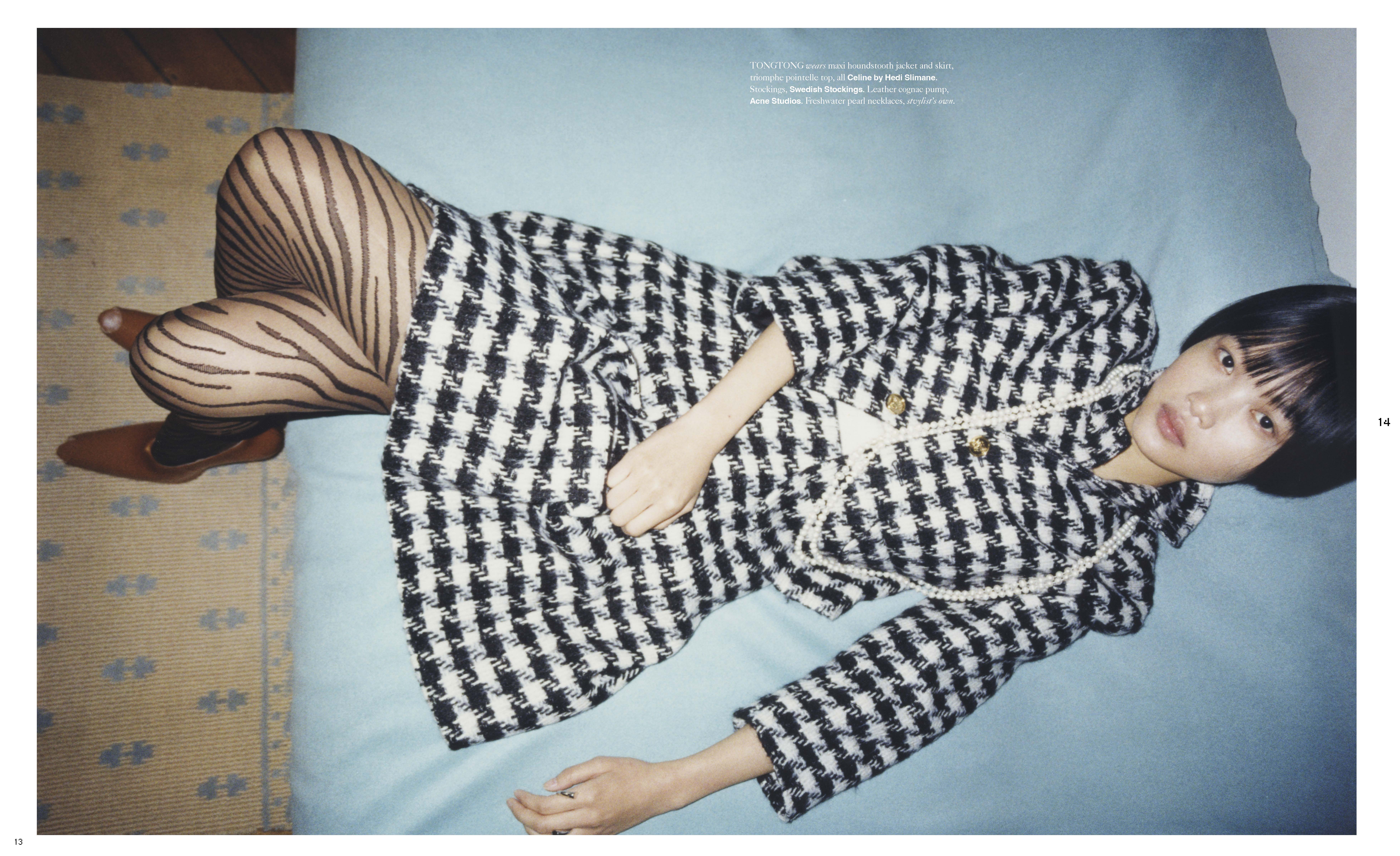 Asian female fashion model in houndstooth jacket and patterned tights lying on a blue bed. Editorial fashion photography. Interior setting.