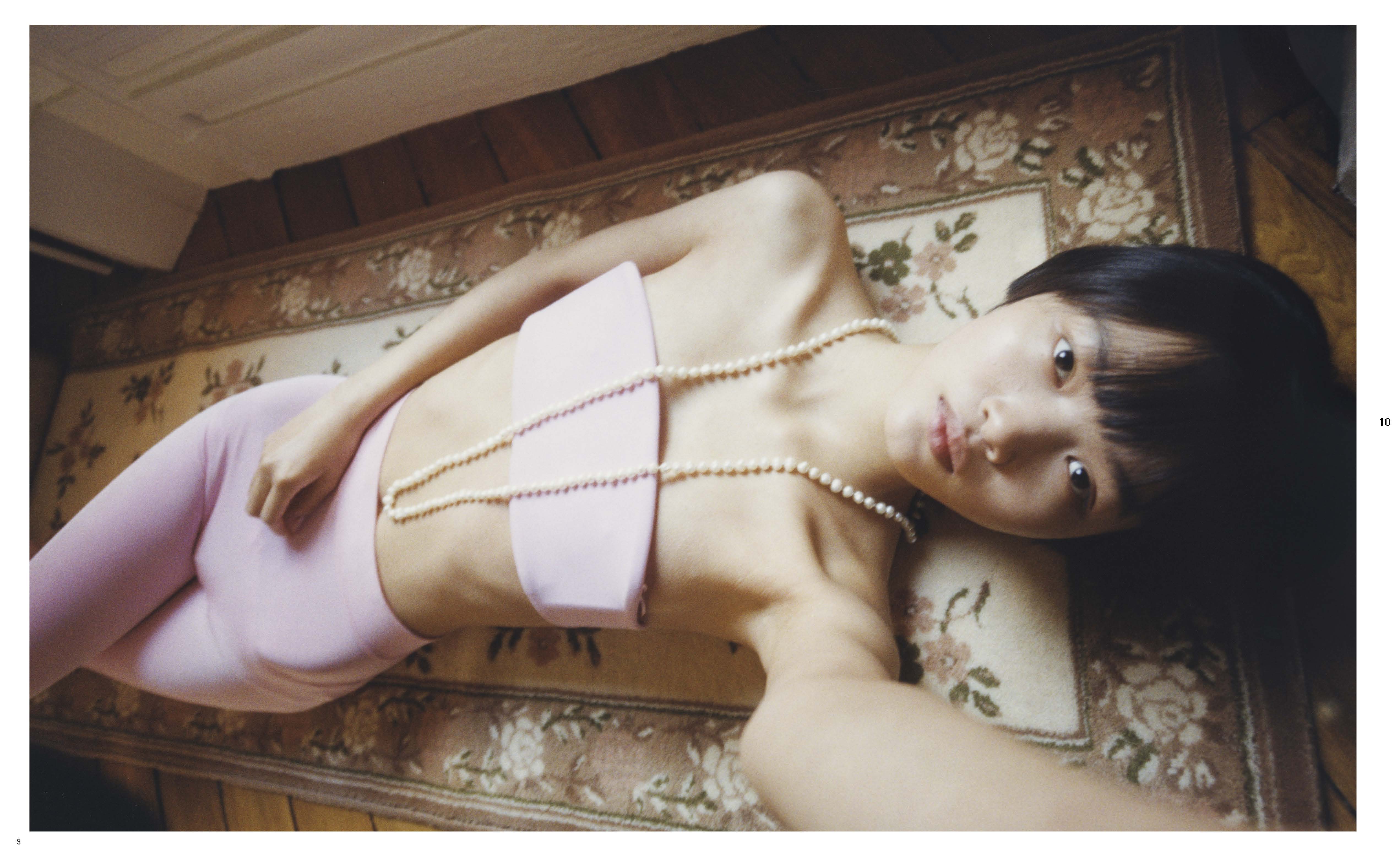 Young adult woman with dark hair laying on a floral rug with pearl necklaces and wearing a pink top and leggings indoors.