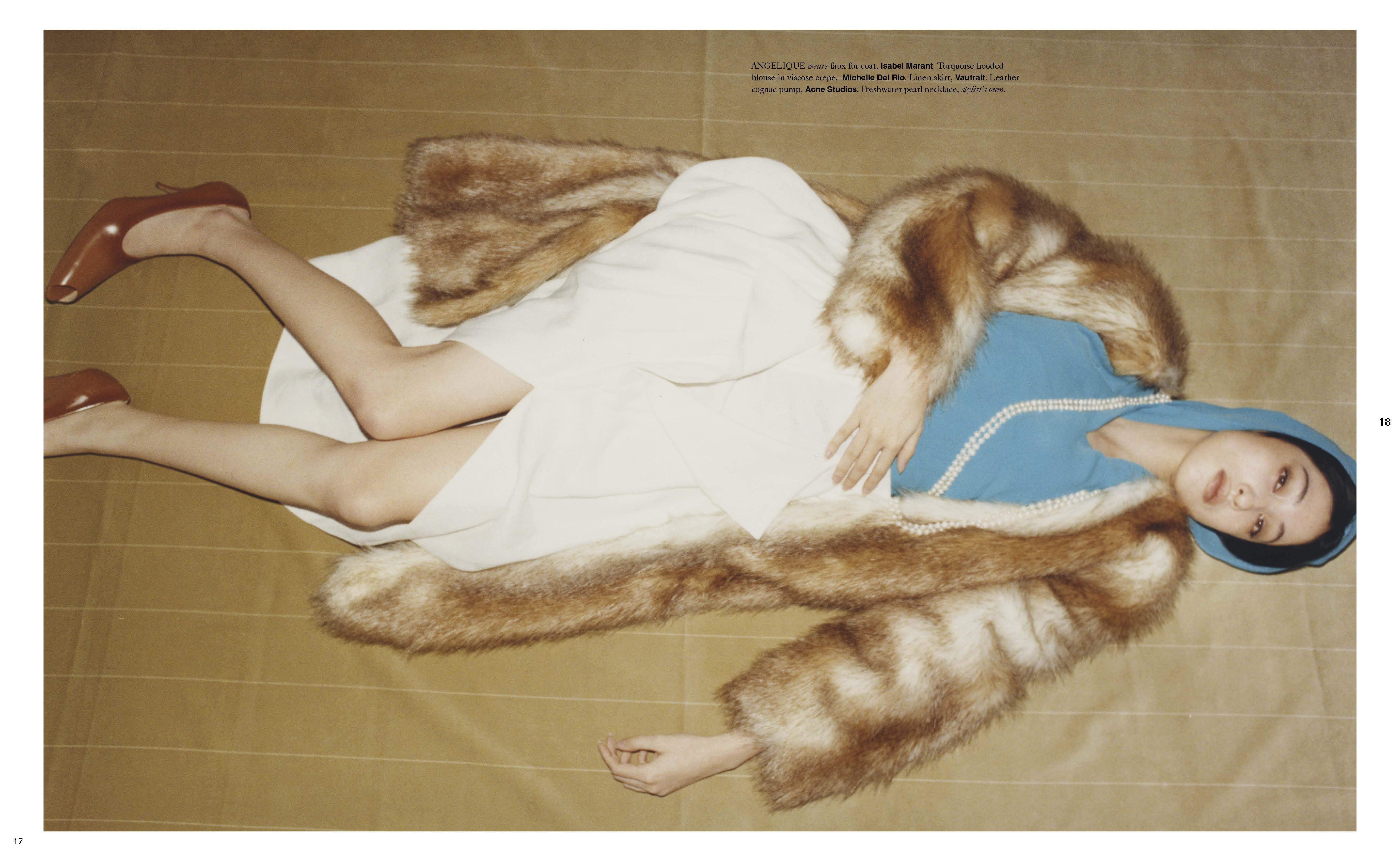 Editorial fashion shot of a woman lying on a gold surface wearing a blue hooded top, white dress, brown heels and faux fur coat.