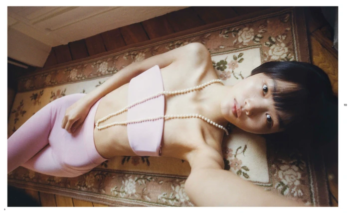 Woman in pink bandeau top and leggings lying on a floral patterned rug with a pearl necklace