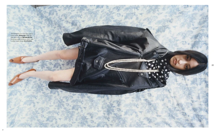 Model lying on a patterned blue-and-white toile fabric background wearing a black leather jacket and brown pumps.
