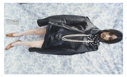 Model lying on a patterned blue-and-white toile fabric background wearing a black leather jacket and brown pumps.
