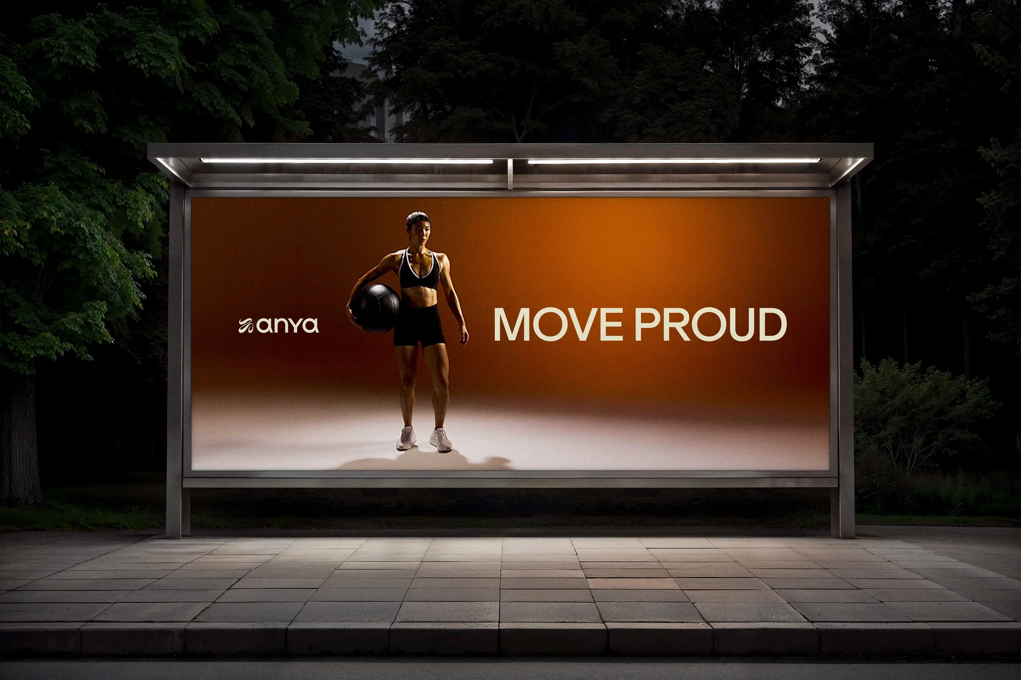A fitness advertisement in a bus shelter at night shows a woman in sportswear holding an exercise ball, promoting a motivational message.