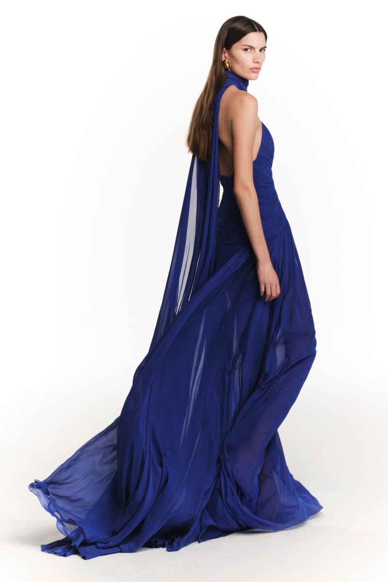 A woman in an elegant, flowing, royal-blue halter dress, posing against a stark white background, showcasing the garment's design and movement.