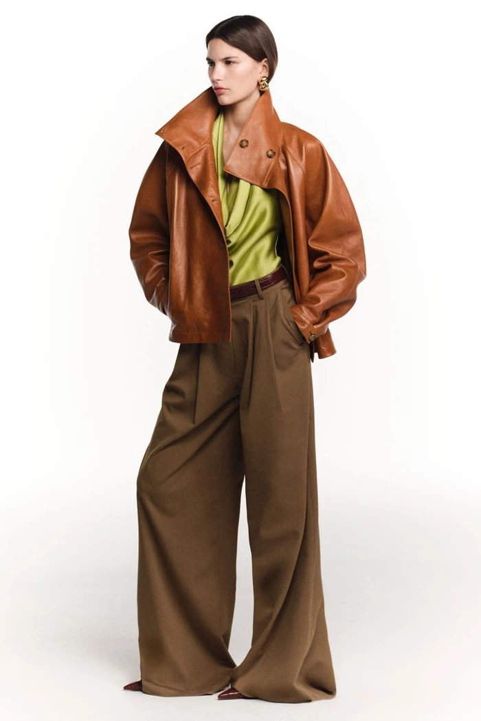 Model in oversized brown leather jacket and wide-legged trousers against a plain white background