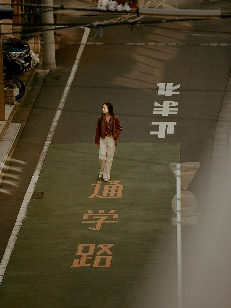 Woman walks on a painted crosswalk in urban setting. Overhead shot captures the scene in neutral colors, featuring street signage.