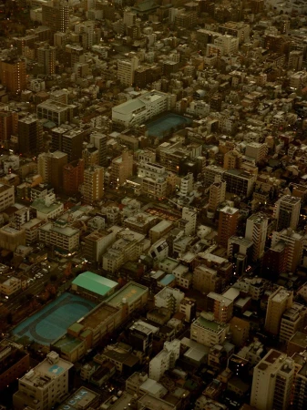 Aerial view of a dense urban landscape featuring numerous buildings with flat roofs, roads, and possibly a school with sports fields in Tokyo.