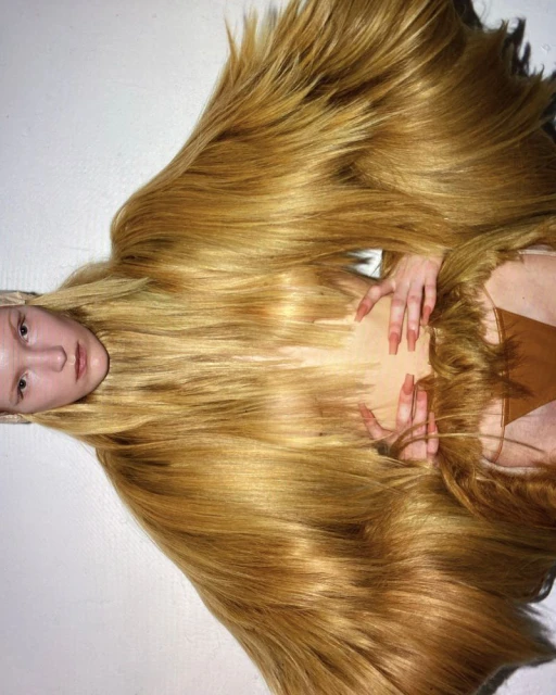 Eye-level studio shot of a young adult woman lying down, surrounded by long, straight blonde hair, creating an abstract, flowing design.