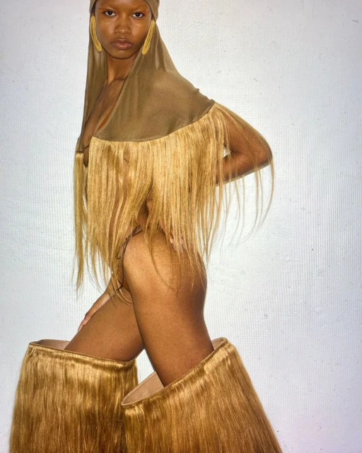 Woman in creative fashion outfit, nude with head covering and fringed top and leg coverings, posing in a photo studio.
