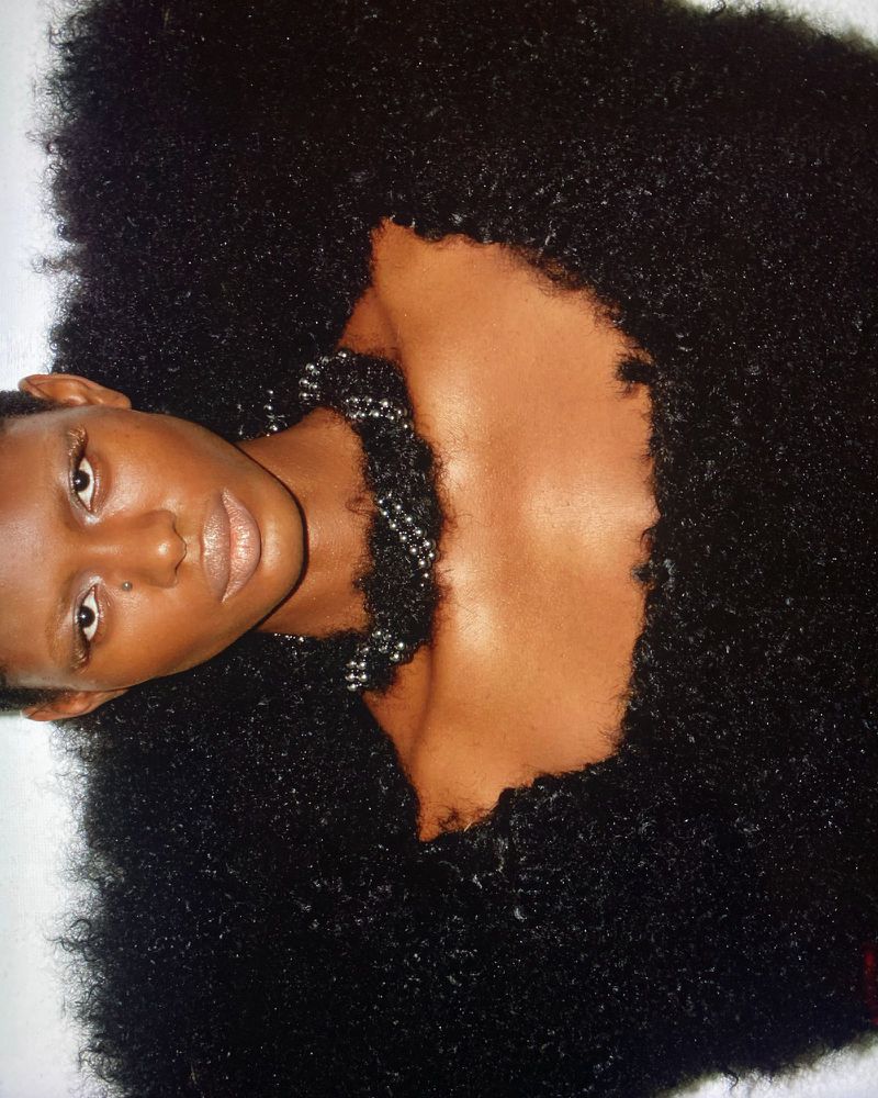Model wearing textured black fluffy couture garment with beaded necklace against white background