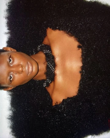 Model wearing textured black fluffy couture garment with beaded necklace against white background
